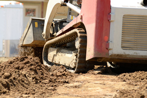 Infrastructure excavation building contractors smoothing dirt over water lines in a utility trench at a commercial residential development